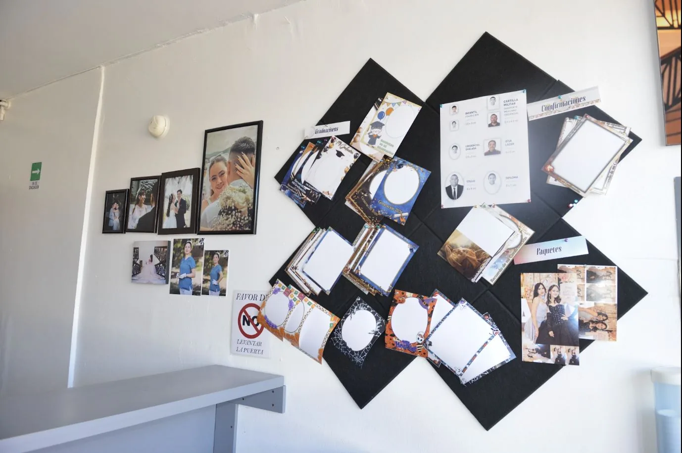 Muro del laboratorio con retratos enmarcados y muestras de paquetes para graduaciones y confirmaciones